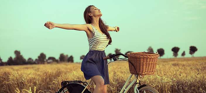 Free woman enjoying freedom on bike on wheat field at sunset